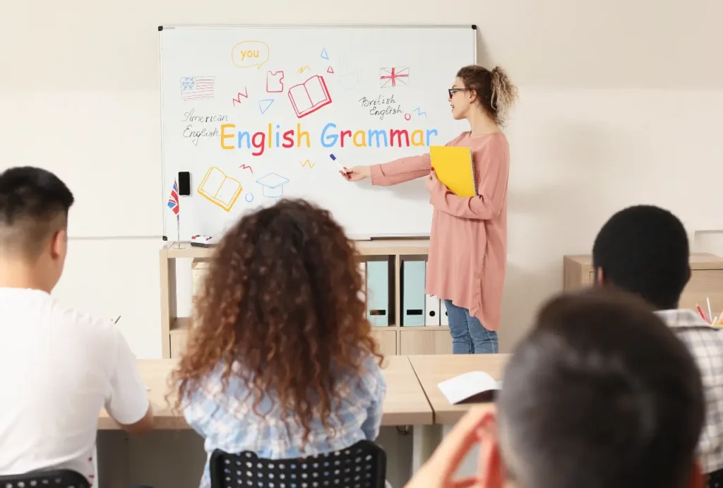 TEFL teacher writing English grammar notes on a whiteboard in front of a class of students